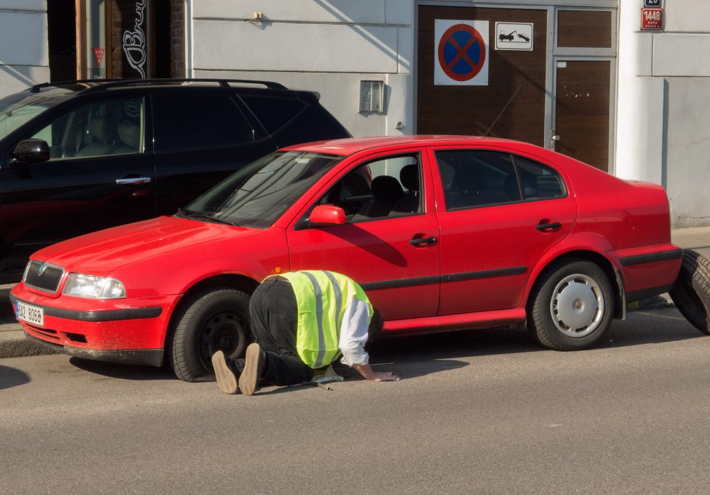 Man changing the punctured tyre on the red car (Škoda Octavia – Czech car). Man in reflex vest changing a wheel. Natural look image of macn repairing car.
Man changing the punctured tyre on the red car. Source: LibreShot